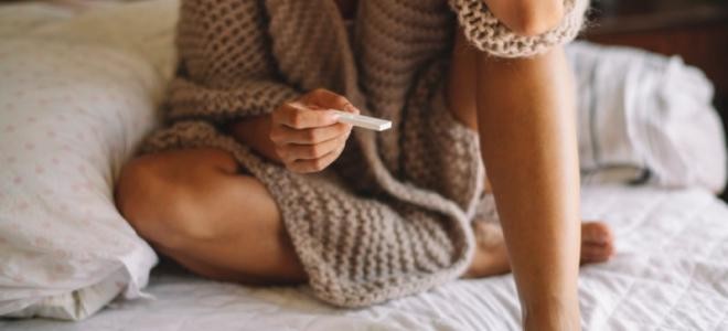 Frau sitzt mit Schwangerschaftstest auf einem Bett
