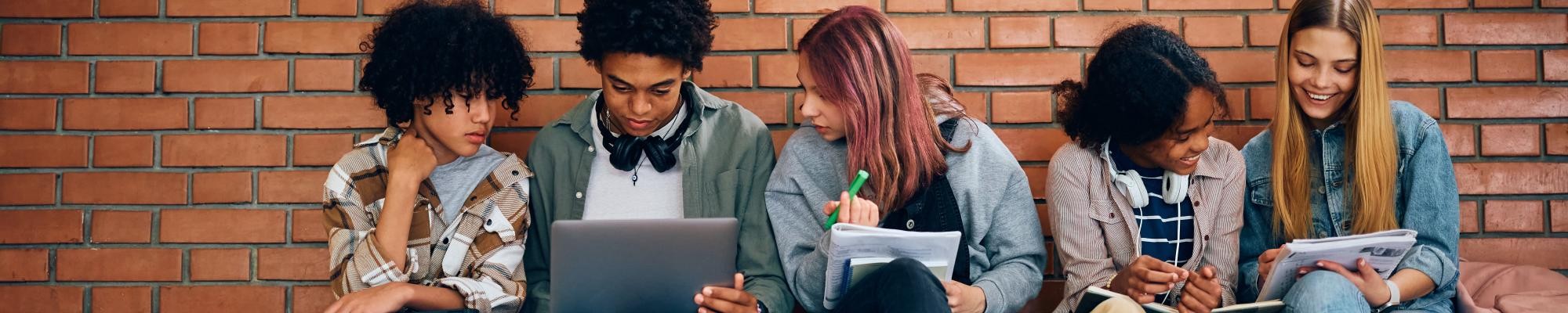 Jugendliche mit Laptop und Heften sitzen nebeneinander